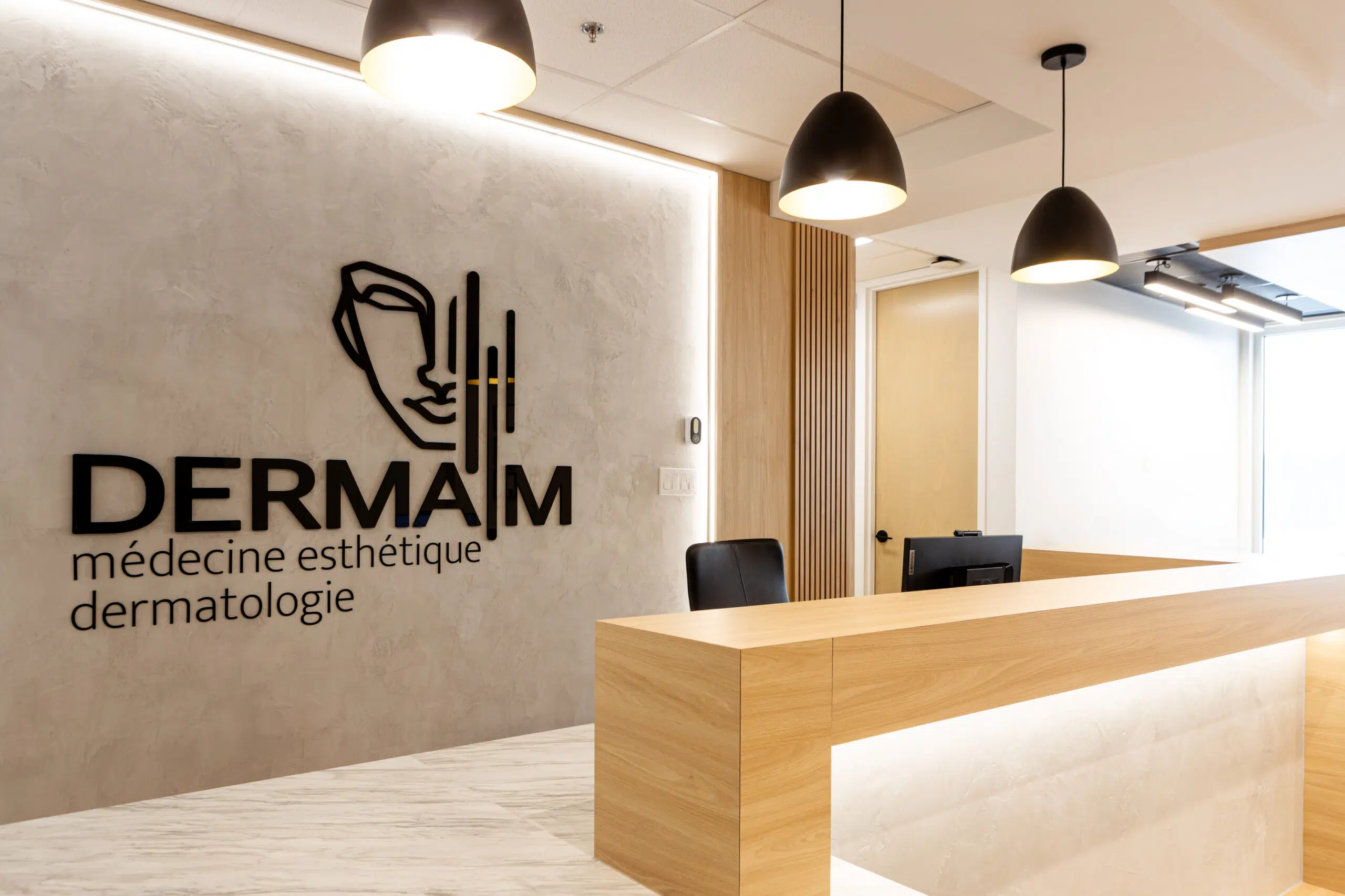 Réception de la clinique Derma M à Trois-Rivières. Une salle lumineuse et moderne avec un mur de béton et un bureau minimaliste en bois clair.